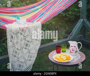 Coin détente dans le jardin. Cadre extérieur en été. Hamac. Tranches d'orange, de verres et de carafe sur une petite table basse. Banque D'Images