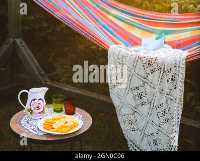 Coin détente dans le jardin. Cadre extérieur en été. Hamac. Tranches d'orange, de verres et de carafe sur une petite table basse. Banque D'Images