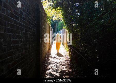 Femme portant une longue jupe de citron et un chapeau de soleil marchant sur Mytten Twitten à Cuckfield près de Haywards Heath , Sussex , Angleterre , Royaume-Uni Banque D'Images