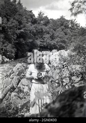 Dans les années 1950, une dame d'un fleuve qui prend une photo à l'aide d'un appareil-photo « box », peut-être un Kodak « Brownie », un appareil-photo amateur populaire de l'époque. Banque D'Images