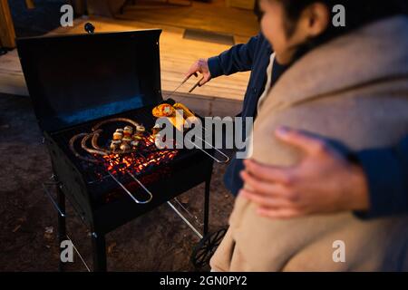 Vue rognée de l'homme qui cuisine sur le gril et de l'embrasser petite amie floue à l'extérieur Banque D'Images