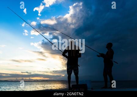 Salvador, Bahia, Brésil - 18 avril 2021 : silhouette de pêcheurs avec leurs poteaux au coucher du soleil. Banque D'Images