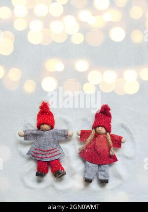 Petites poupées de Noël ornements faisant des anges dans la neige comme s'ils étaient des enfants avec des lumières bokeh. Copier l'espace Banque D'Images