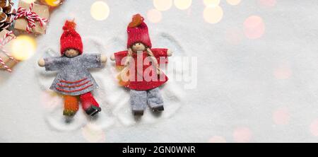 Petites poupées de Noël ornements faisant des anges dans la neige comme s'ils étaient des enfants avec des lumières bokeh et des cadeaux. Copier l'espace Banque D'Images