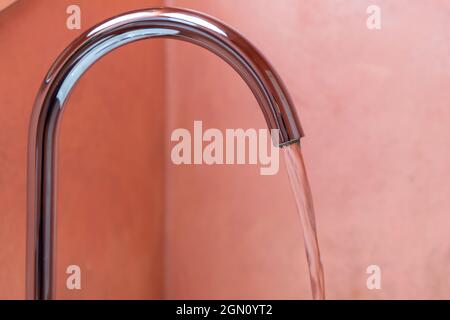 De l'eau coule d'un robinet en acier brillant dans une salle de bains, gros plan photo Banque D'Images