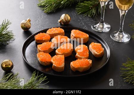 Canape de Noël festive avec caviar rouge sur ciabatta sur fond noir. Fête des fêtes. Gros plan. Banque D'Images