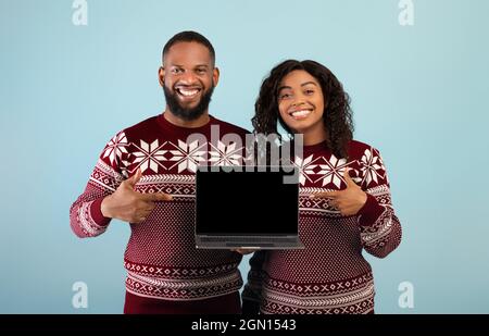 Achats en ligne de Noël. Un heureux couple afro-américain montrant un ordinateur portable avec un écran vide, pointant dessus Banque D'Images