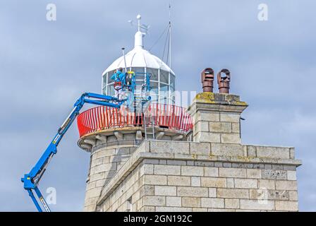 Des ouvriers, utilisant une perche articulée, repeignant le phare de Howth, Dublin, Irlande. Banque D'Images