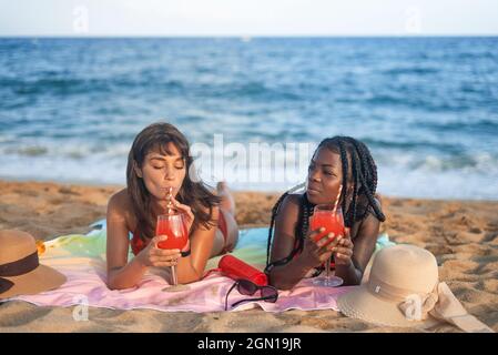 Jeunes femmes diverses se détendant sur une plage de sable et buvant des cocktails tout en passant des vacances d'été ensemble sur la mer Banque D'Images