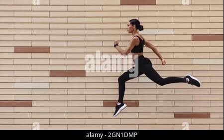 Motivation sportive. Athletic Young Woman in Sportswear running sur fond de mur de briques Banque D'Images