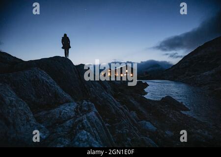 Homme se tient devant la cabane de montagne la nuit dans les montagnes suisses, Suisse, chaîne de montagnes, alpinisme, Banque D'Images
