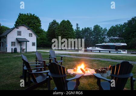 Des chaises entourent les feux de camp au terrain de camping de Parcs Canada, à Beveridge Locks, sur la rivière Tay, avec une péniche le Boat Horizon au crépuscule, près de Lower R Banque D'Images