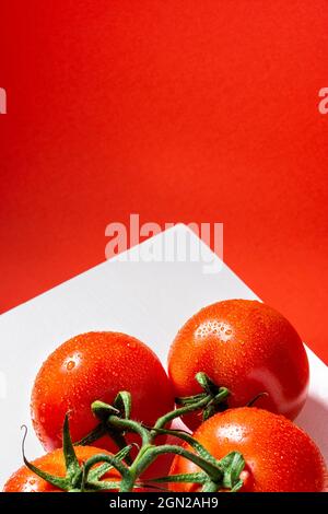 Gros plan d'un groupe de quatre tomates rouges naturelles humides sur une table blanche et un fond rouge. La photo dispose d'un espace de copie et cette photo est prise en position verticale Banque D'Images