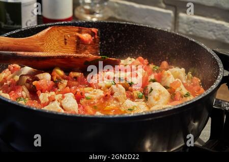 Le poisson-bar avec tomates fenouil et basilic est frit dans une casserole sur le poêle à gaz. Banque D'Images