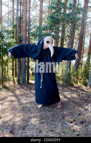 Un homme dans un masque de médecin de la peste se tient dans la forêt contre les arbres de fond Banque D'Images