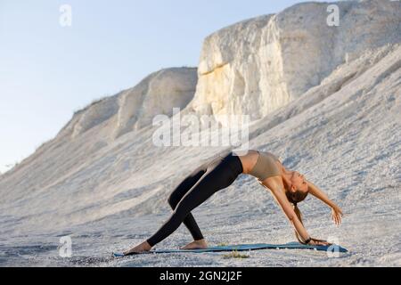 Jeune femme pratiquant le yoga sur les falaises blanches le matin. Le yoga sauvage pose contre le coucher du soleil. Banque D'Images