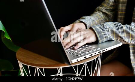 Gros plan des mains d'une femme dans une veste dactylographiant sur un ordinateur portable. La personne travaille, étudie à la maison en ligne. Pas de face. Banque D'Images