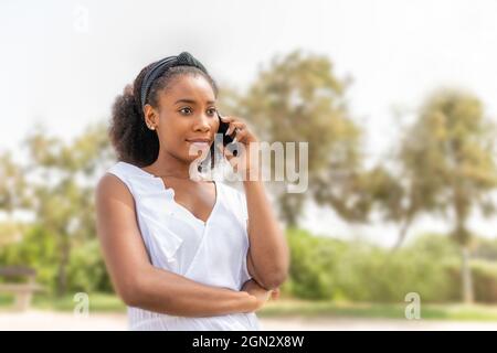 Une jeune femme afro-américaine parle avec son téléphone dans le parc Banque D'Images