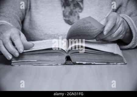 Une femme assise à une table lit et retourne à travers un livre. Mise au point sélective. Photo en noir et blanc Banque D'Images