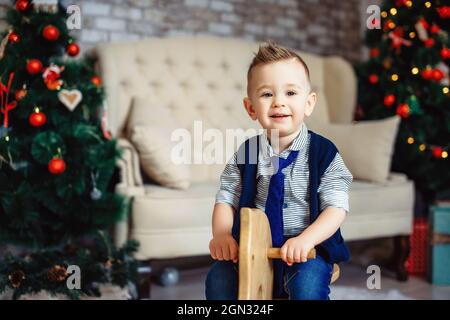 Souvenirs joyeux des vacances de Noël pour les enfants. Adorable garçon élégant dans une cravate à cheval en bois à bascule. Joyeux petit enfant élégant. Banque D'Images