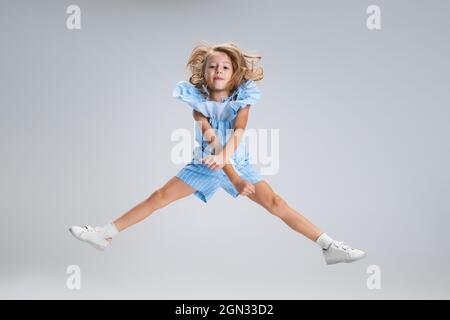 Portrait complet d'une jolie fille dans des vêtements décontractés sautant isolés sur fond blanc de studio. Concept d'enfance heureuse. Enfant ensoleillé. Semble heureux Banque D'Images