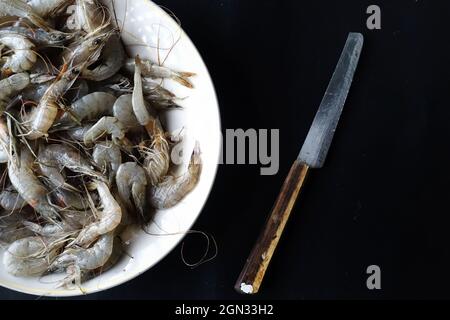 bouquet de crevettes crues sur une assiette blanche et un couteau isolé sur fond noir Banque D'Images