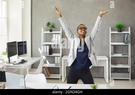 Une femme afro-américaine joyeuse danse sur le lieu de travail célèbre la promotion Banque D'Images