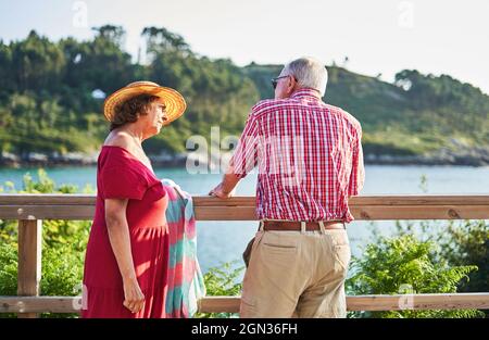 Couple senior se tenant à proximité et regardant l'un l'autre tout en appréciant la vue sur la mer par jour ensoleillé Banque D'Images