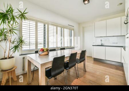 Salle à manger contemporaine et cuisine intérieure avec table contre four intégré et hotte au-dessus de cuisinière dans la maison lumineuse Banque D'Images