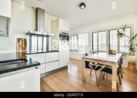 Salle à manger contemporaine et cuisine intérieure avec table contre four intégré et hotte au-dessus de cuisinière dans la maison lumineuse Banque D'Images