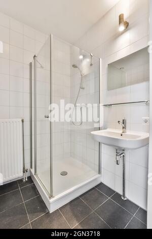 Intérieur de la salle de bains avec miroir suspendu sur le lavabo placé près de la porte d'entrée et cabine de douche en verre dans l'appartement moderne Banque D'Images