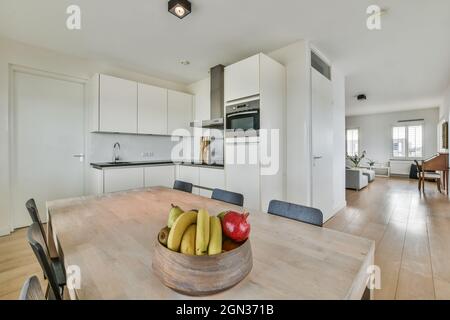 Salle à manger contemporaine et cuisine intérieure avec table contre four intégré et hotte au-dessus de cuisinière dans la maison lumineuse Banque D'Images