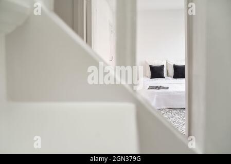 Vue à travers la main courante de l'escalier sur la porte à la chambre avec lit blanc et coussins noirs dans la maison Banque D'Images