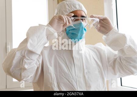 Homme adulte médique dans un équipement de protection individuelle mettant des lunettes de protection tout en regardant vers l'avant à l'hôpital Banque D'Images