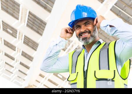 De dessous de la personne mature heureux de l'ethnie superviseur mâle dans la veste de mise sur hardhat tout en regardant loin à proximité de la centrale solaire Banque D'Images