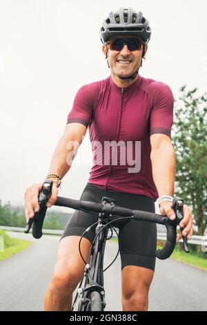 Joyeux sportif adulte en vélo lunettes de soleil et casque assis sur la route à vélo sur la route de campagne en plein jour Banque D'Images