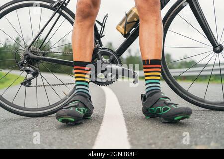 Niveau du sol de l'athlète masculin sans visage dans des chaussures de cyclisme et des chaussettes rayées debout sur la route avec vélo Banque D'Images