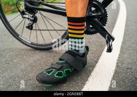 Niveau du sol de l'athlète masculin sans visage dans des chaussures de cyclisme et des chaussettes rayées debout sur la route avec vélo Banque D'Images