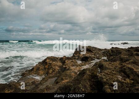 Vue panoramique sur la mer ondulée avec eau mousseuse coule sur la plage rugueuse avec la montagne en Cantabrie Espagne Banque D'Images