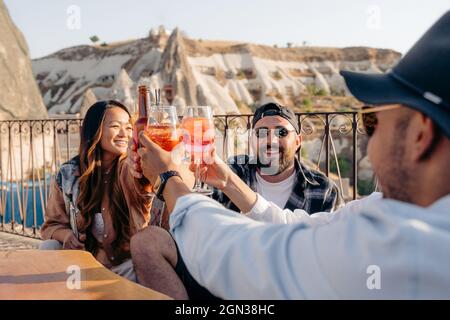 Des amis souriants assis autour d'une table et levant des verres de cocktails tout en vous accrochant au bar Banque D'Images