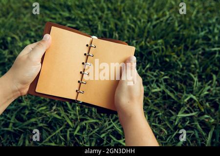 ouvrez le carnet en cuir marron dans ses mains sur un fond d'herbe verte Banque D'Images