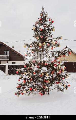 Arbre de noël décoré de boules dorées et rouges et étincelant de neige sur le sapin pendant la neige en plein air. Noël avec de la neige. Joyeux Noël Banque D'Images