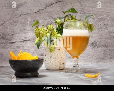 Verre de bière avec une branche de houblon et un bol avec des chips de pomme de terre sur le fond de pierre grise. Banque D'Images