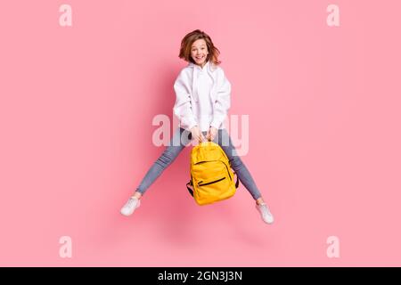 Pleine longueur taille fille saut en haut de garder sac d'école heureux gai isolé pastel couleur rose fond Banque D'Images