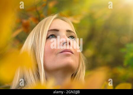 Portrait d'une belle jeune femme dans la nature, encadrée par des feuilles d'automne d'or défocused, regardant dans les rayons de lumière douce et chaude du soleil Banque D'Images