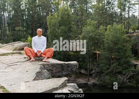 méditation bouddhiste pieds nus tout en étant assis sur une falaise rocheuse au-dessus d'un lac forestier Banque D'Images