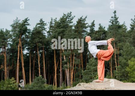 vue latérale de la pose d'un arc debout bouddhiste pratiquant sur une falaise rocheuse en forêt Banque D'Images