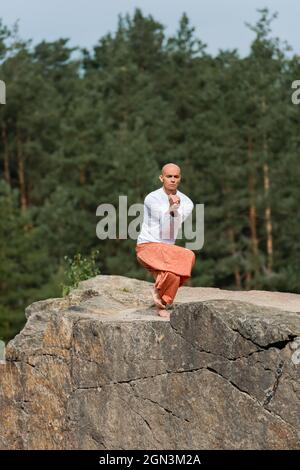 un sweat-shirt blanc bouddhiste pieds nus pratiquant le yoga pose sur le rocher en forêt Banque D'Images