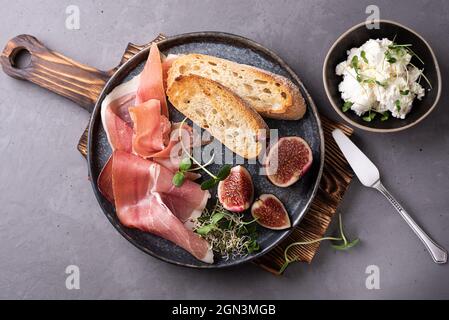Prosciutto avec tranches de pain et figues sur une assiette sur fond de béton, antipasti italiens avec fromage à la crème, gros plan. Banque D'Images