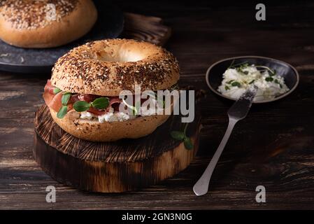 Sandwich avec ricotta, prosciutto et microverts, bagel de jambon pour le petit déjeuner sur un fond de bois sombre, style rustique. Banque D'Images